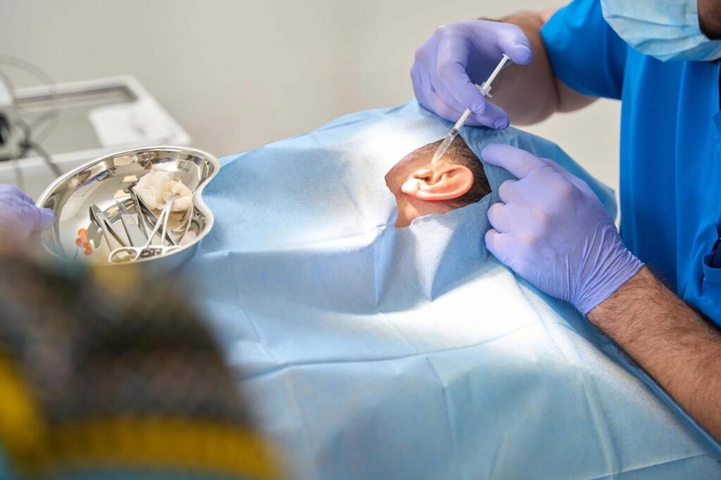 ENT specialist performing ear treatment procedure and medical injection near the ear in a clinical operation setup.